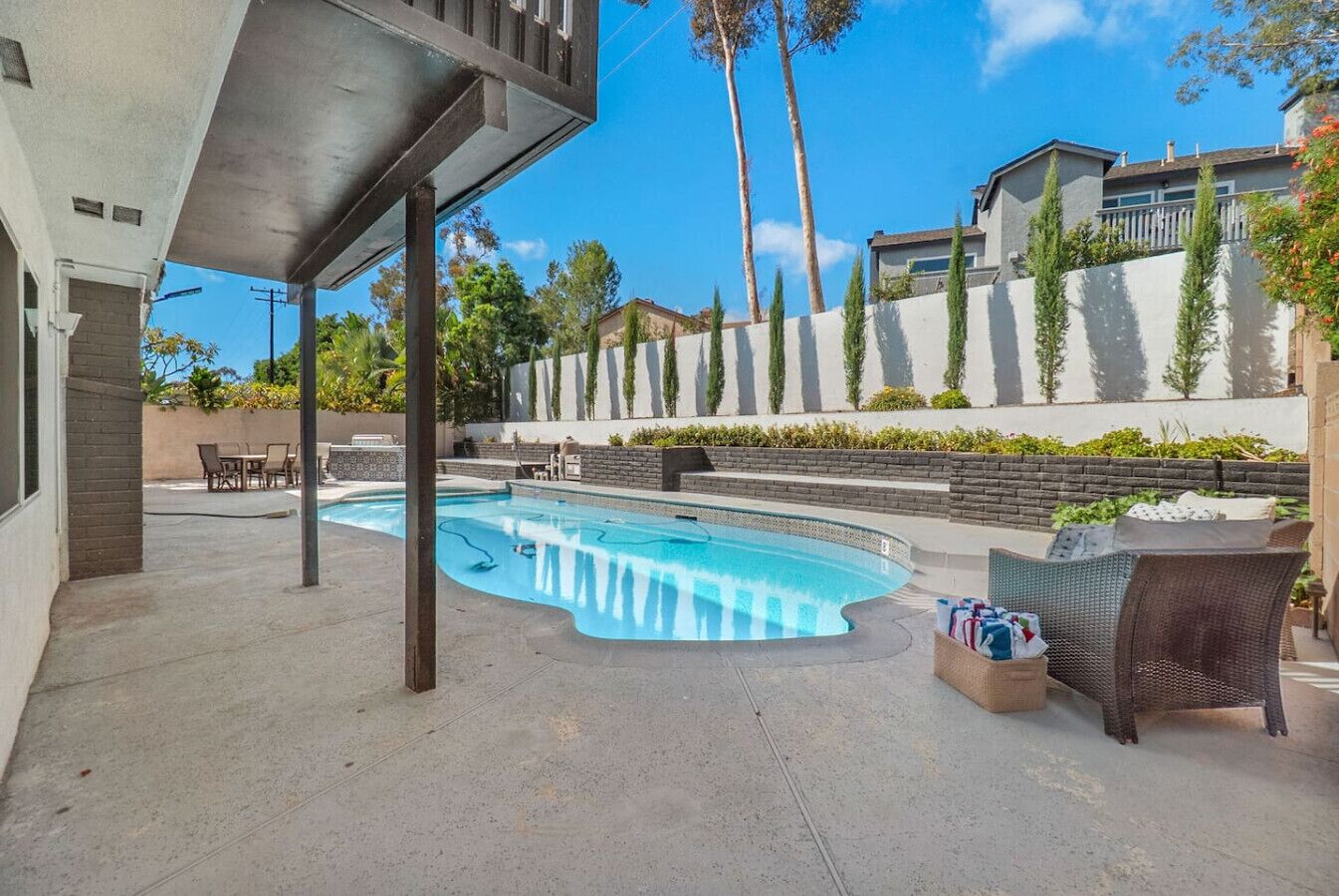 Piscina de borde curvo, rodeada por una terraza con mobiliario exterior y un muro de piedra.