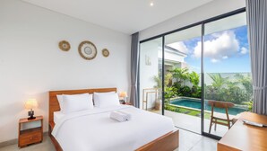 A modern hotel room with a large bed, a desk, and a view of a swimming pool. - Famiglie Guest House (Munggu)