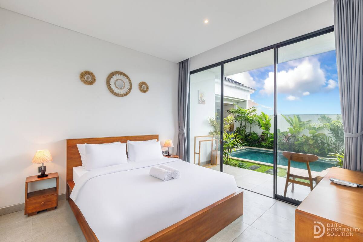 A modern hotel room with a large bed, a desk, and a view of a swimming pool.