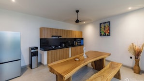A modern kitchen with wooden cabinets, a stainless steel refrigerator, and a wooden dining table with benches. - Famiglie Guest House (Munggu)