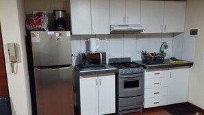 A compact kitchen with a refrigerator, microwave, stove, and sink. - Charming 1-bedroom apartment in Surco with AC, two blocks from American Embassy (Santiago de Surco)