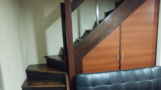 A staircase with wooden steps leading to a room with a wardrobe and a black leather sofa. - Charming 1-bedroom apartment in Surco with AC, two blocks from American Embassy (Santiago de Surco)