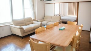 A room with a wooden dining table, beige sofa, and a bed with curtains. - THE HORAI (Hakodate)