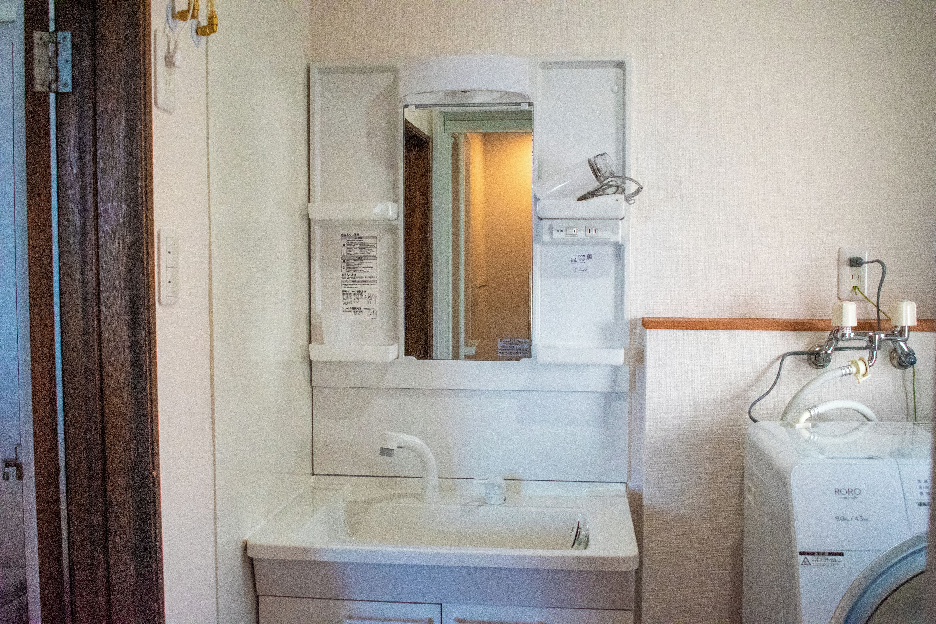 Een kleine badkamer met een wit wastafel, een spiegel en een inbouw wasmachine.