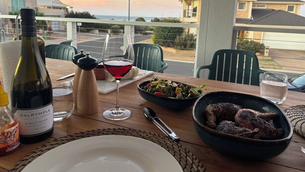A dining table with a bottle of wine, a glass of red wine, a bowl of salad, and a plate.