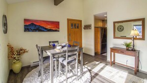 A dining area with a table set for four, a wooden door, a mirror, and a painting of a mountain landscape.