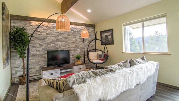 A living room with a stone wall, a television, a sofa, and a hanging chair.