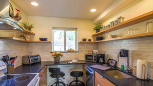 A modern kitchen with a central island, bar stools, a toaster, a microwave, and various kitchen appliances.