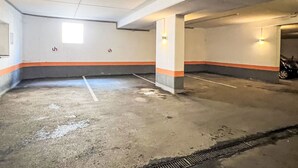 An indoor parking garage with concrete floors, marked parking spaces, and orange and gray painted walls. - Apartment Studio by Interhome (Oberndorf in Tirol)