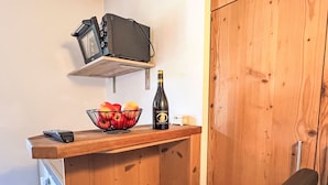 A small kitchenette with a wooden countertop, a bowl of fruit, a bottle of wine, and a black chair.