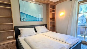 A bedroom with a bed, wooden headboard, built-in shelves, and a large window.