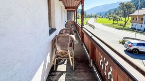 A balcony with wicker chairs, a wooden ceiling, and a view of a road and mountains. - Cheeky Apartment by Interhome (Oberndorf in Tirol)