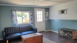 A living room with a sofa, a wooden chest, and a window with curtains. - Explore the Owyhee River, Leslie's gultch,  Three Forks, lava tubes and more. (Jordan Valley)