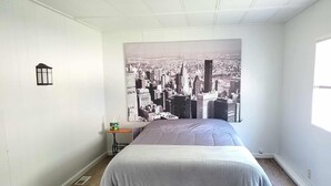 A bedroom with a cityscape mural, a bed, a small table with a lamp, and a window. - Explore the Owyhee River, Leslie's gultch,  Three Forks, lava tubes and more. (Jordan Valley)