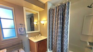A bathroom with a vanity, a large mirror, a shower curtain, and a towel rack with towels. - Explore the Owyhee River, Leslie's gultch,  Three Forks, lava tubes and more. (Jordan Valley)