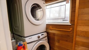 A laundry area with stacked washing machines, a window, and a wooden wall.