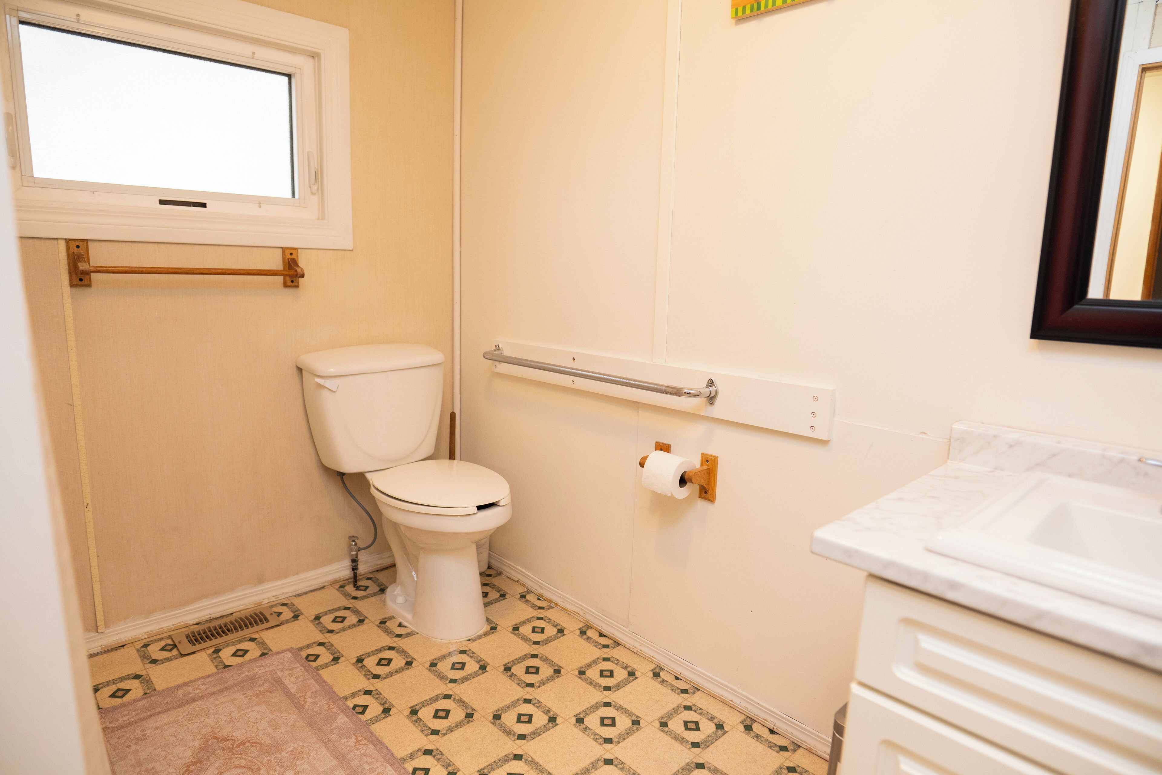 A bathroom with a toilet, a sink, a window, and a patterned floor.