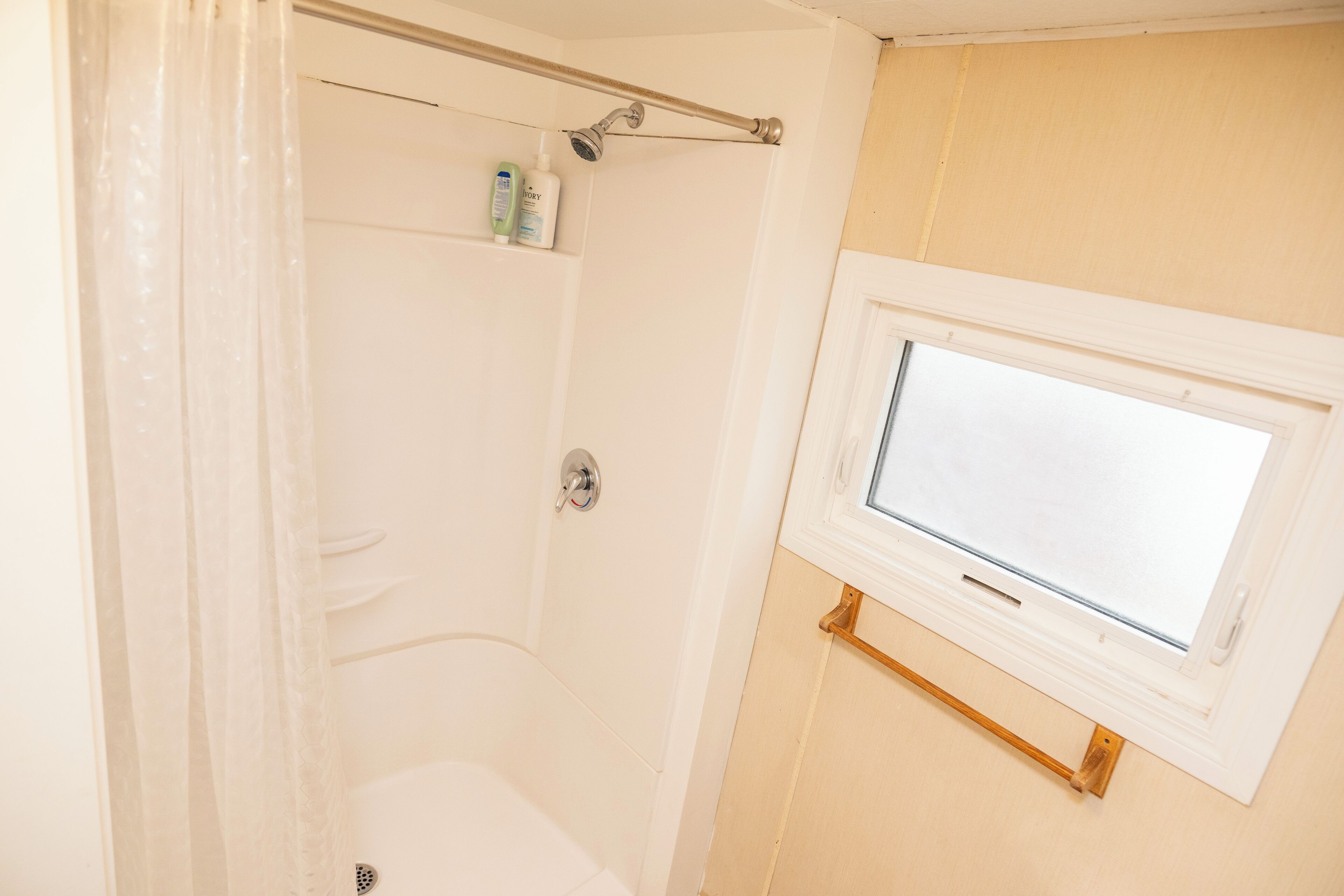 A bathroom with a shower, a window, and a towel rack.
