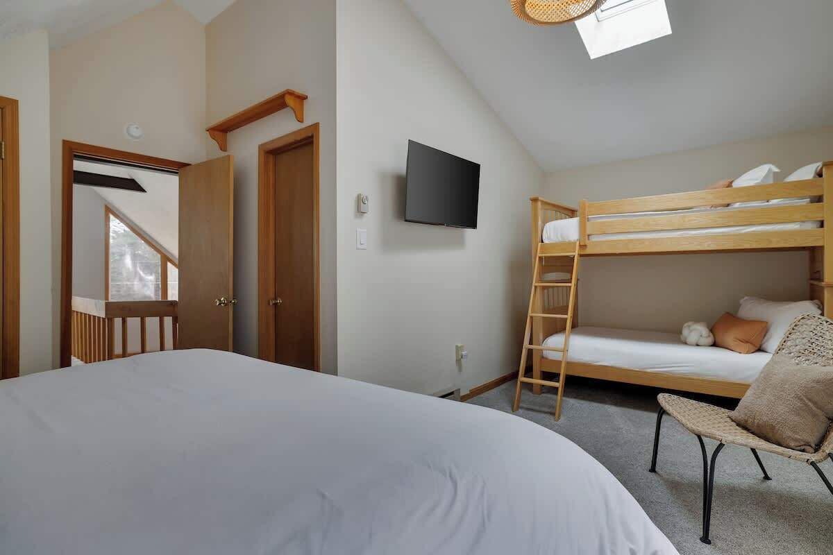 Un dormitorio con literas, una silla, un televisor y una puerta que da a otra habitación.