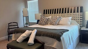 Une chambre à coucher comprenant un lit, un banc, une chaise, un ventilateur de plafond et une fenêtre avec des stores.