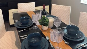 Une table à manger dressée avec des assiettes, des verres et des couverts bleu foncé, une bougie et une bouteille de vin.