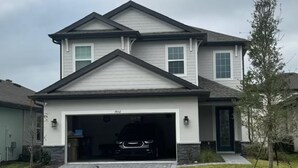 Une maison à deux étages avec un garage, une allée et un oiseau perché sur les marches.
