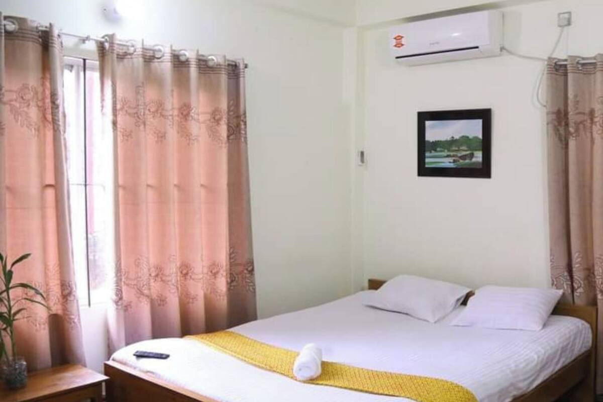 A bedroom with a bed, a bedside table, a potted plant, and an air conditioning unit on the wall.
