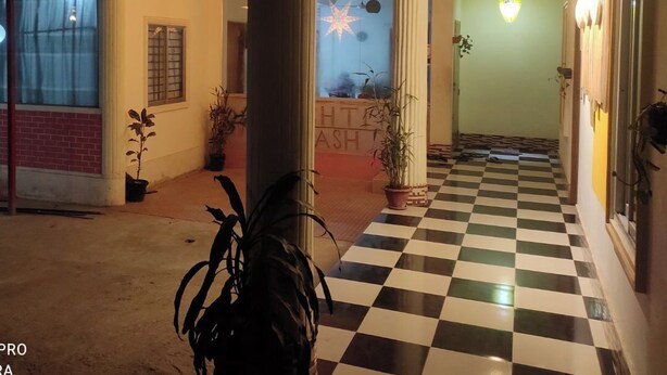 A hotel corridor with checkered flooring, potted plants, a star-shaped light fixture, and a visible sign with letters. - Brishti Bilash Guesthouse (Kamalganj)