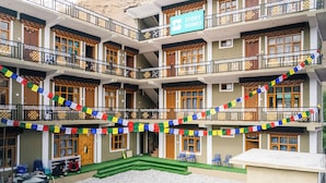 A multi-story hotel with a sign reading "Story Homes." It features balconies with railings, multiple windows, and a courtyard with chairs and a small table. - Story Homes (Kaza)