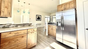 Eine moderne Küche mit Holzschränken, einem Edelstahlkühlschrank und Pendelleuchten.