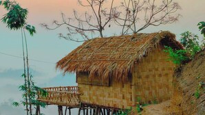 A traditional bamboo house with a thatched roof, elevated on stilts, surrounded by bamboo and trees. - Mirinja Valley Megh Machang Resort (Lama)