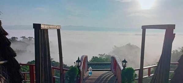 Un puente de madera que conduce a un mirador elevado, con vistas despejadas del paisaje y montañas lejanas.