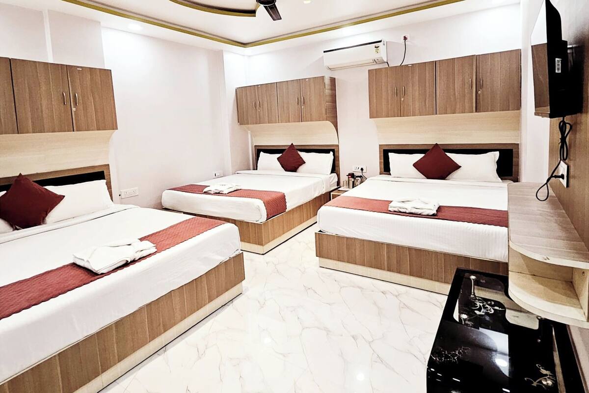 Ein Hotelzimmer mit drei Betten, Holz Kopfteilen, weißen Wänden, einem Deckenventilator und einem Marmorboden.