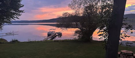Vista de un lago con un muelle, una mesa de picnic y un árbol grande.