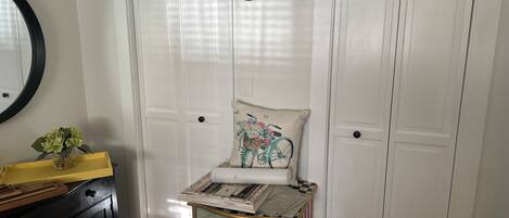 A room with a television mounted on the wall, a decorative cabinet with a landscape painting, a yellow tray with a vase of flowers, and a door with a white panel design.
