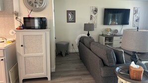 Ein Wohnzimmer mit grauem Sofa, Fernseher, einer Uhr und einer Mikrowelle auf einem Schrank.