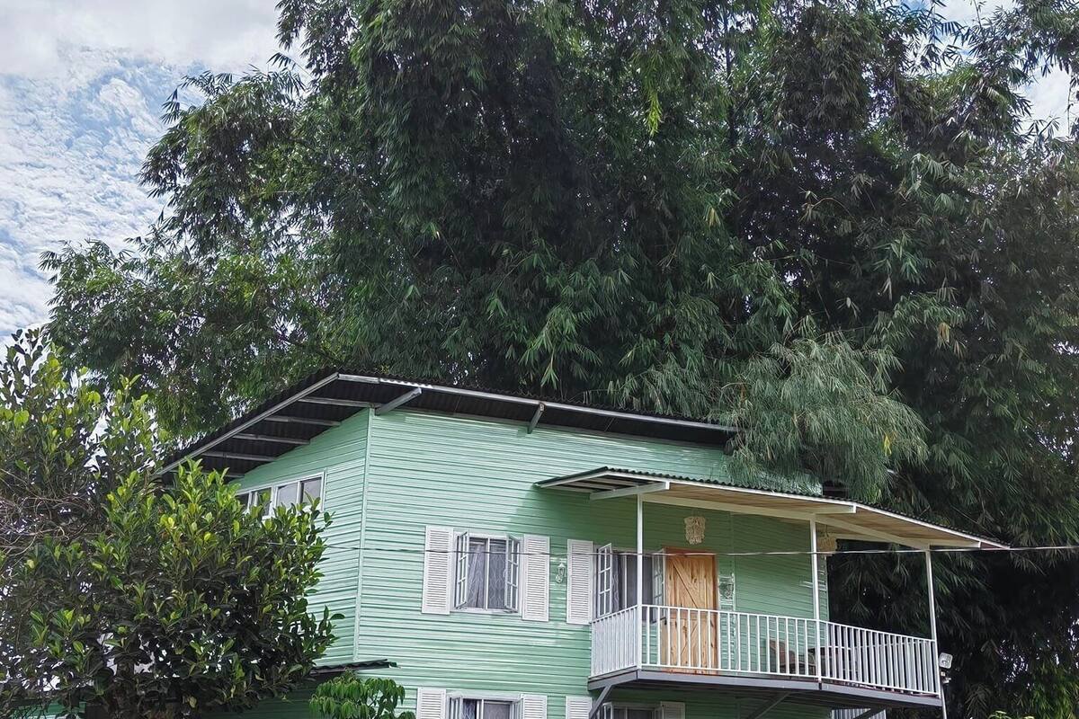 Una casa de dos plantas con balcón, rodeada de abundante vegetación y árboles.