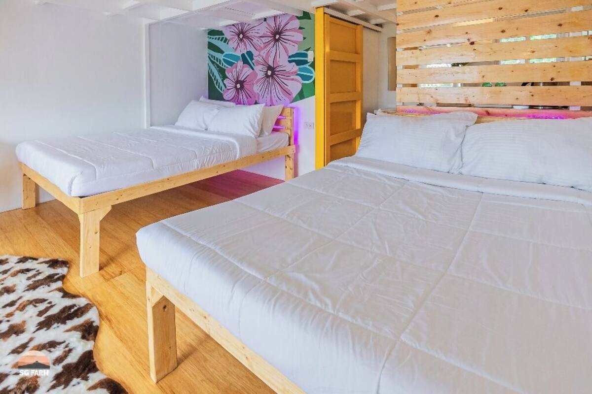 Una habitación con dos camas, cabecera de madera, un mural floral de colores y una pared de listones de madera.