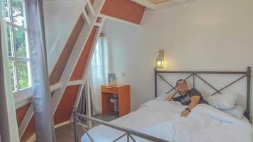 A bedroom with a metal bed frame, a wooden ceiling with exposed beams, a small bedside table, and a window with curtains.