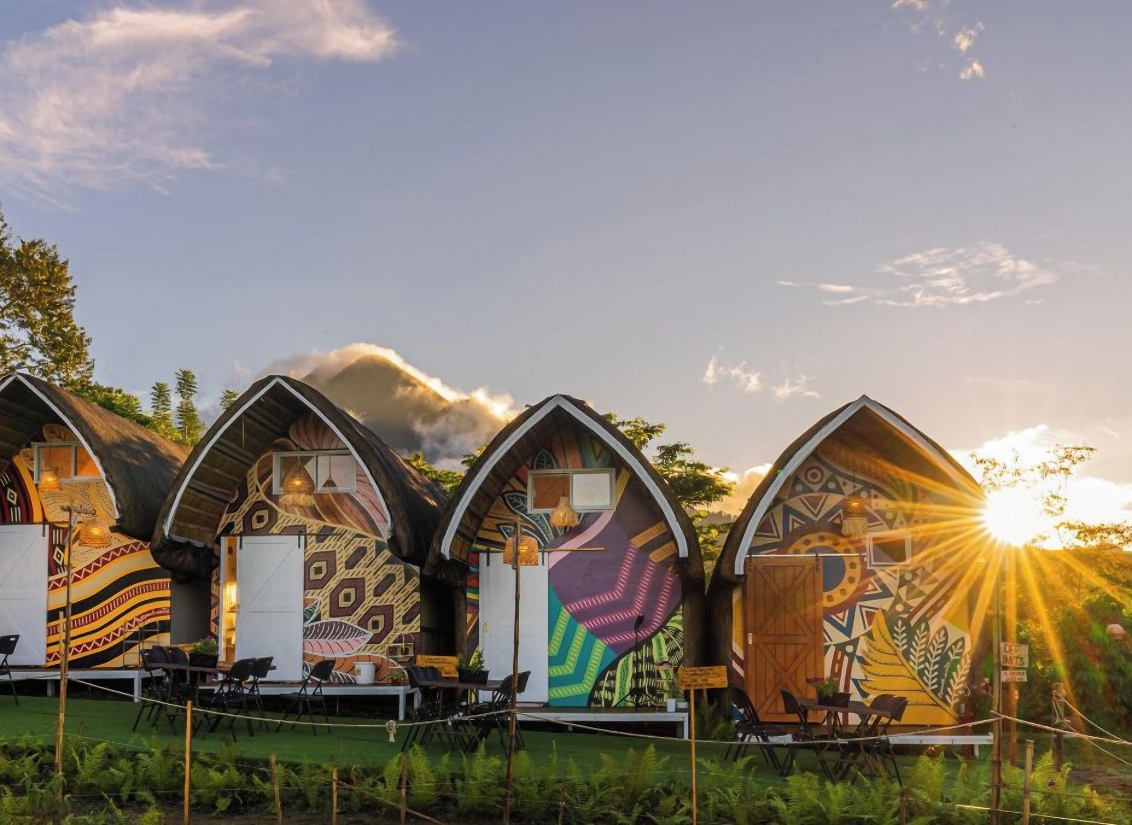 Four unique, arched-roofed cabins with colorful murals, arranged in a row with outdoor seating.