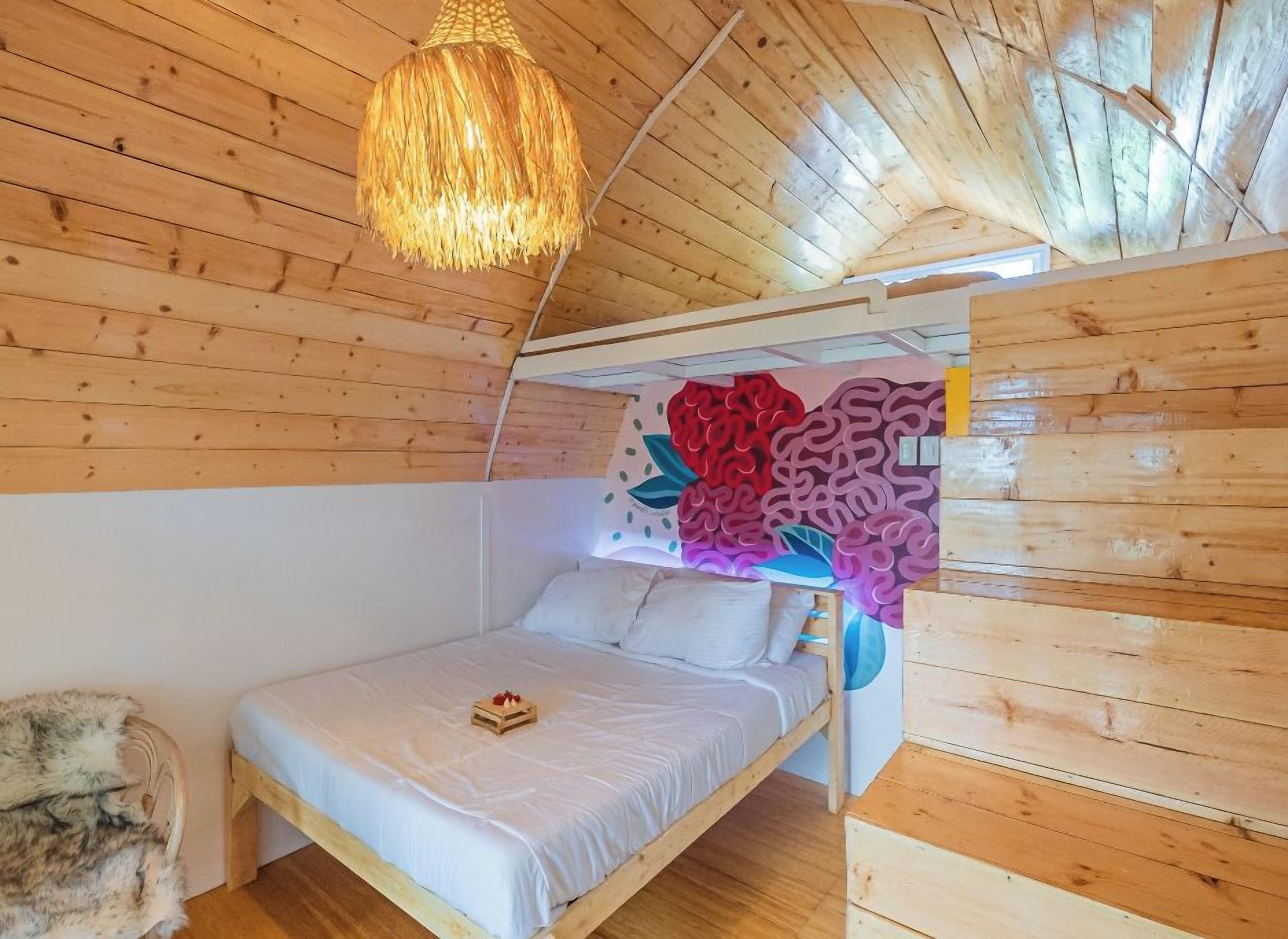 Un dormitorio de cabaña de madera con una cama, una lámpara colgante y un mural en la pared.