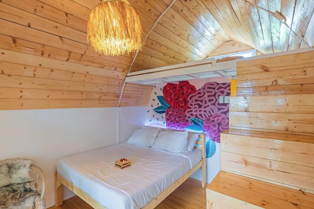 A wooden cabin bedroom with a bed, a hanging light fixture, and a wall mural.