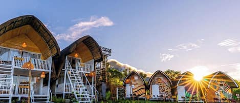 A row of unique, curved-roofed cabins with outdoor seating areas, surrounded by lush greenery.