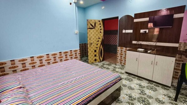 A bedroom with a bed, a wardrobe, a television, and a door leading to another room. - Masum Guest House (Digha)
