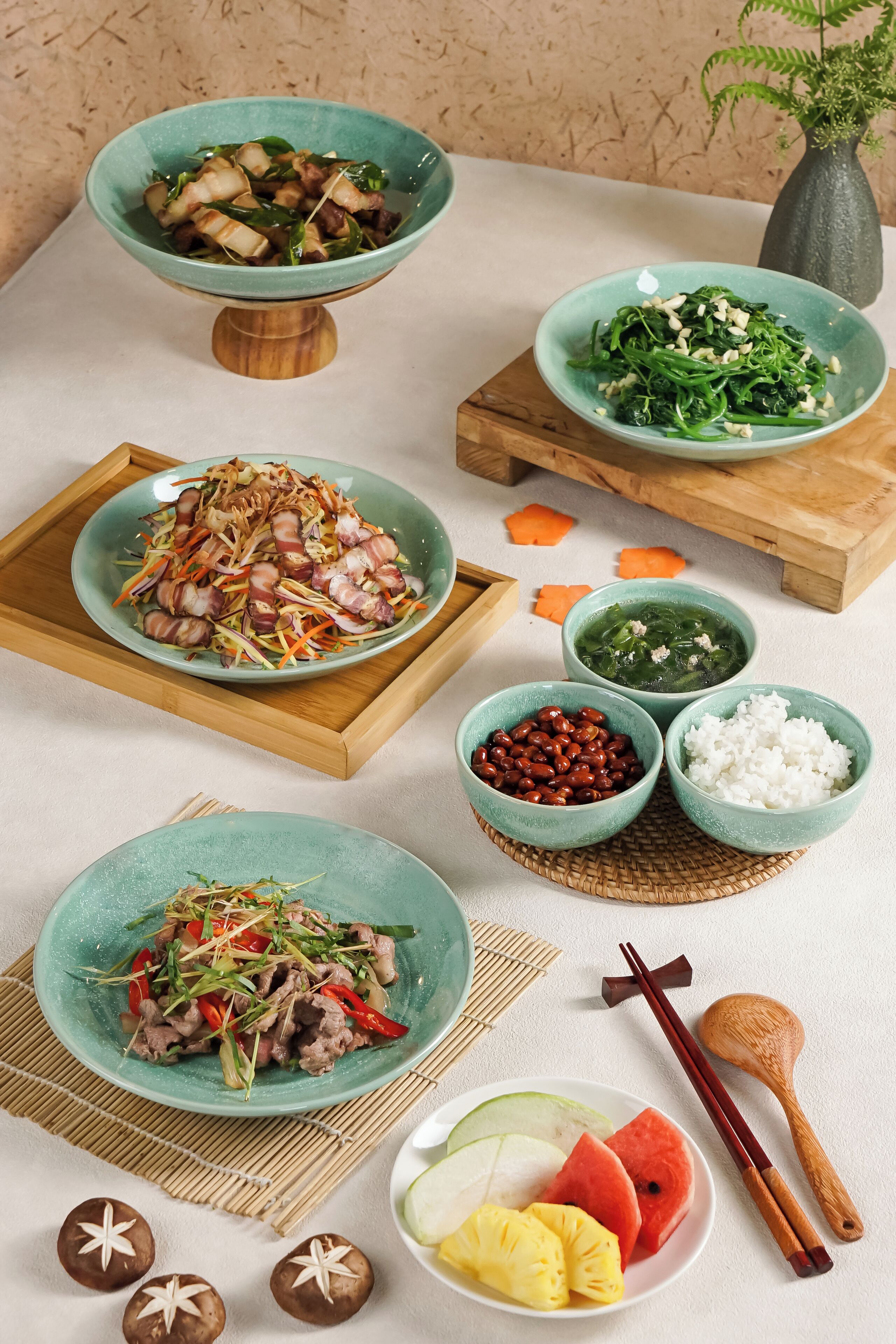 A variety of dishes on a table, including a bowl of sliced meat, a bowl of greens, and a bowl of beans.