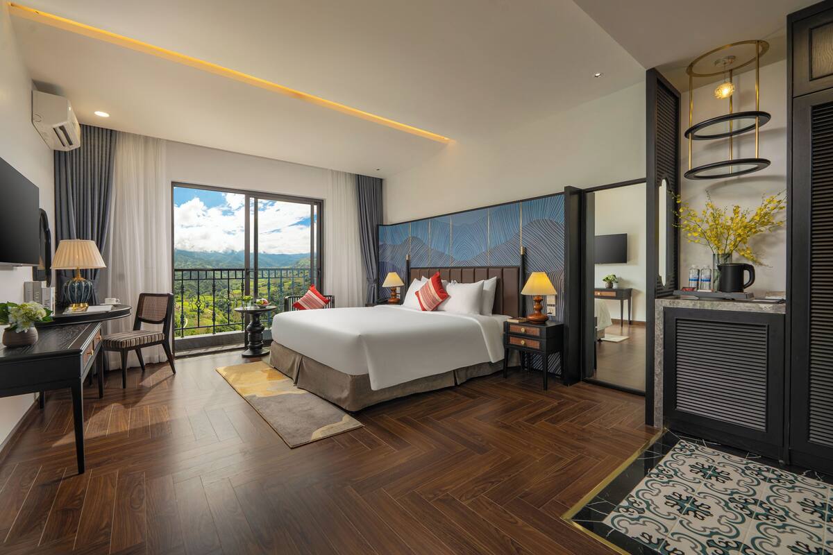 A modern hotel room with a large bed, a desk, a chair, and a view of the outdoors.