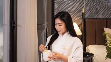 A woman in a white robe sitting by a window with a tray of food and a candle.