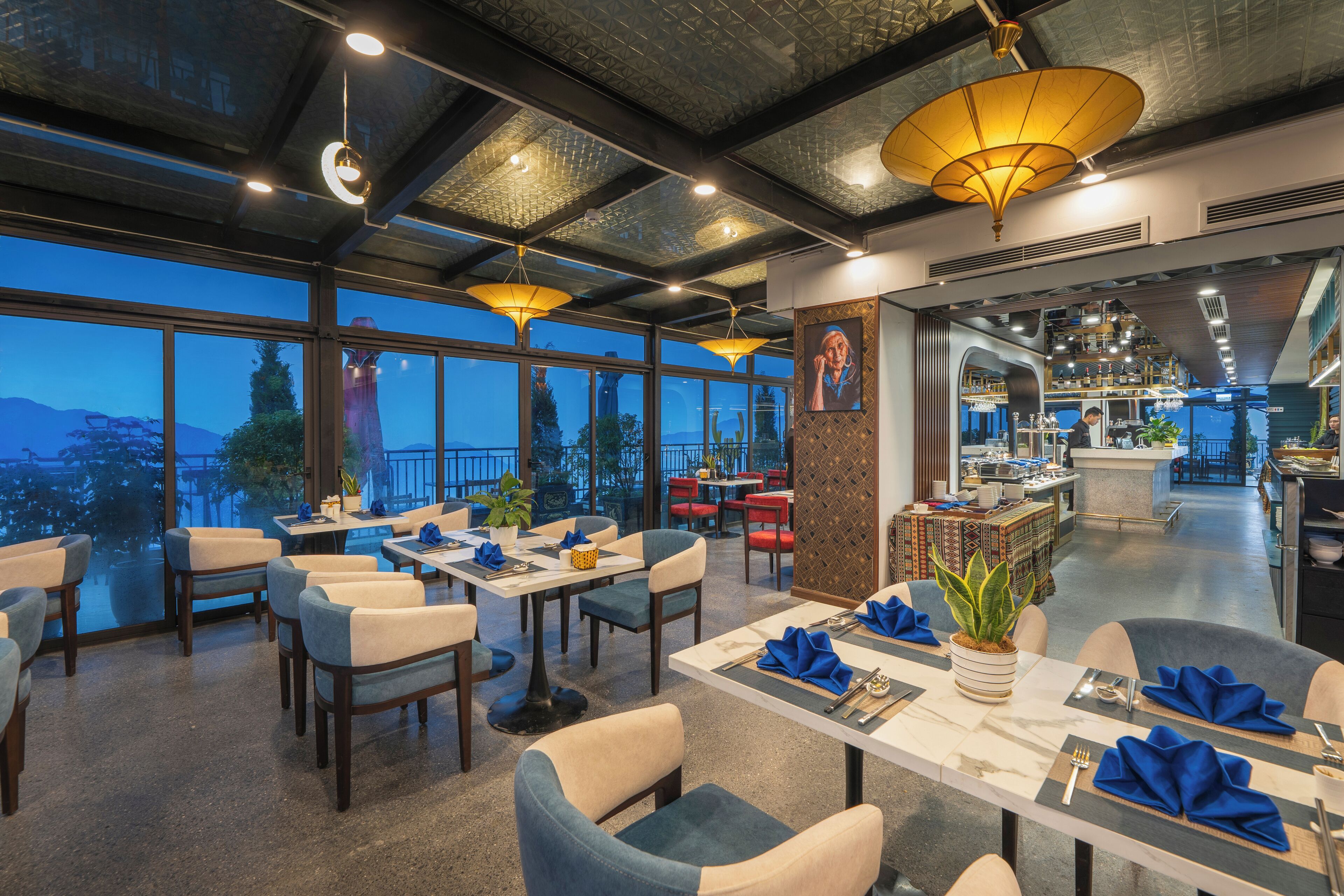 Un restaurante con mesas dispuestas para comer, grandes ventanales que ofrecen una vista y una zona de bar al fondo.