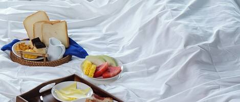 A person in a white robe sitting on a bed with breakfast items including toast, eggs, and fruit.