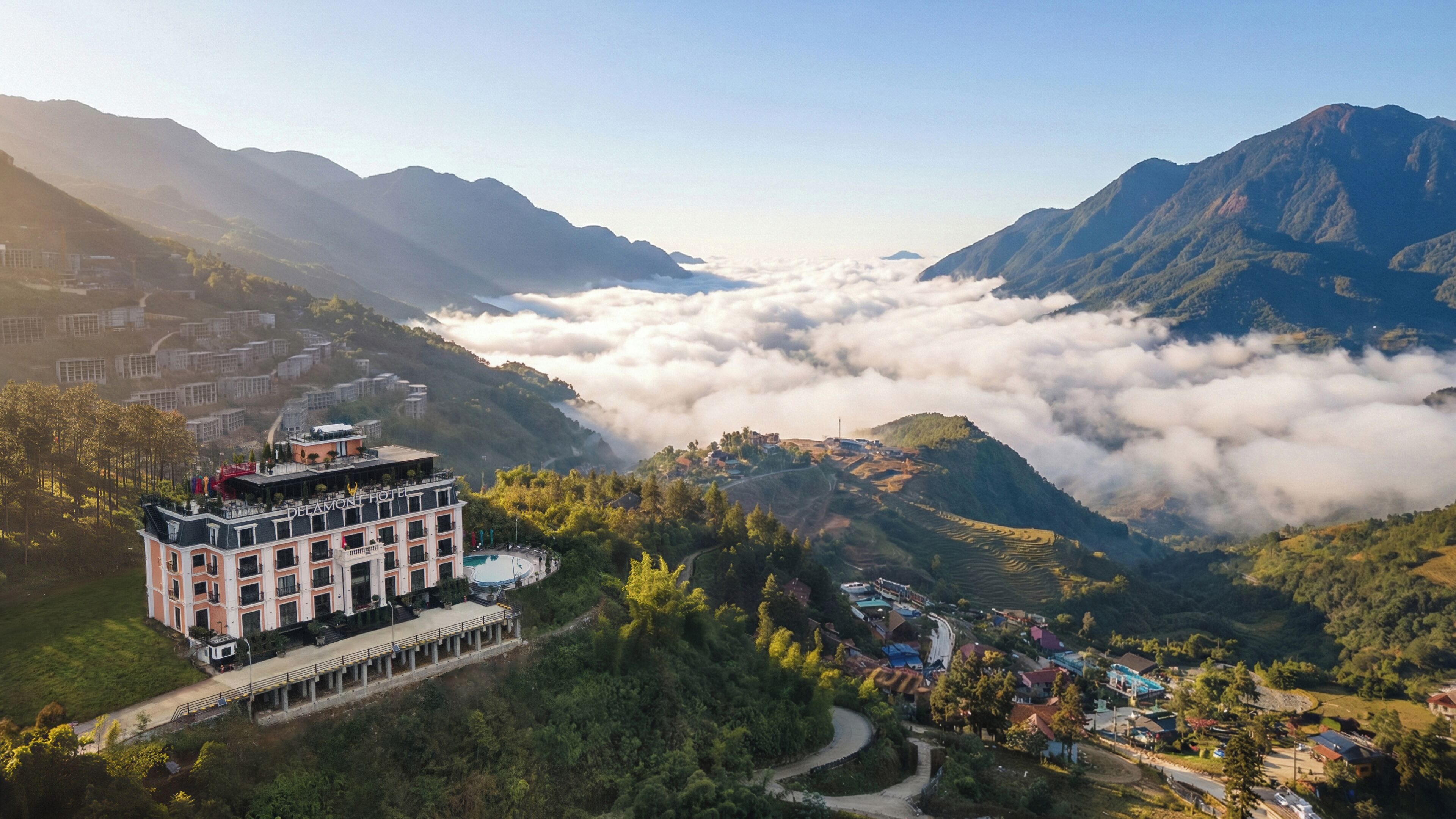 A hotel with a terrace and pool, surrounded by lush greenery and mountains.